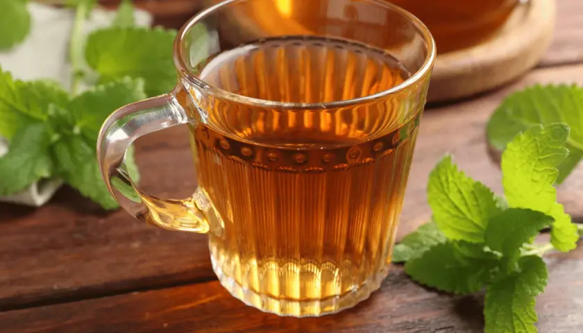 Une tasse de thé ambré, ornée de feuilles de mélisse fraîche, sur une table en bois.