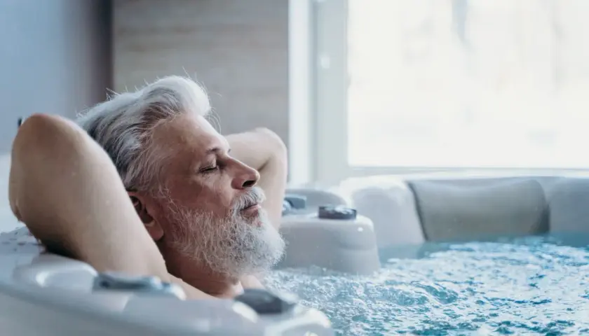 Un homme âgé se détend dans un jacuzzi, les yeux fermés. Il semble si paisible, on se demande si on peut faire du spa tous les jours.
