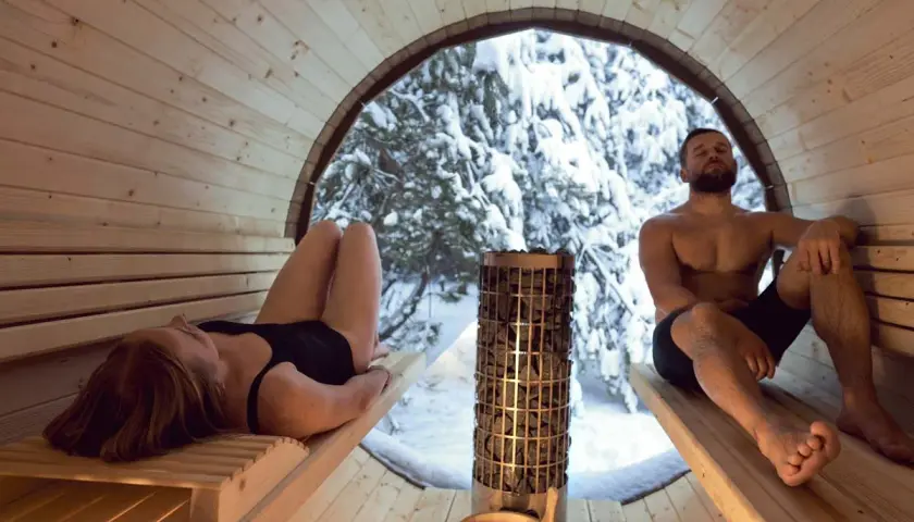Couple se détendant dans un sauna en bois, avec vue sur une forêt enneigée. Le sauna tous les jours danger, mais ici, c'est un moment de pur bien-être.