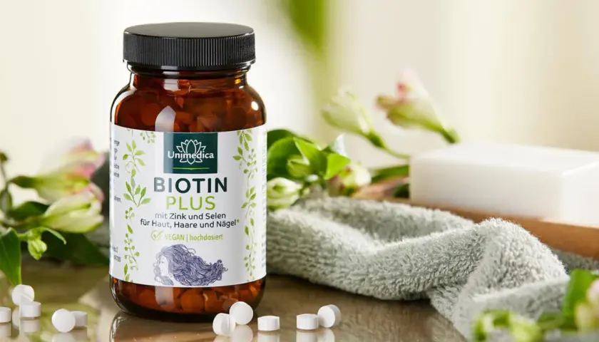 Bouteille de Biotin Plus, un supplément de vitamine B7, entourée de fleurs et d'une serviette douce. Idéal pour la peau, les cheveux et les ongles.