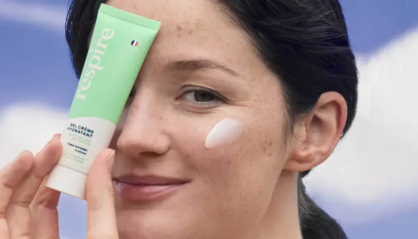 Une femme applique une crème hydratante sur sa joue. Le tube "Respire" est tenu près de son visage, montrant comment hydrater sa peau.