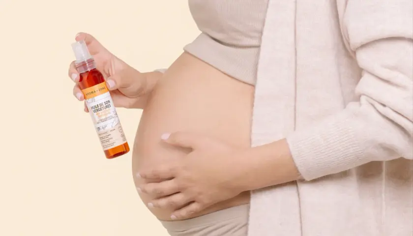 Une femme enceinte tient une huile de soin pour vergetures, idéale pour la grossesse. Le rooibos, ingrédient naturel, prend soin de la peau.