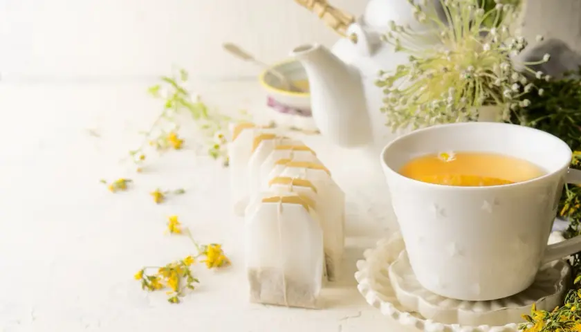 Une tasse de thé ou tisane pour la santé, entourée de fleurs sauvages et de sachets de thé.