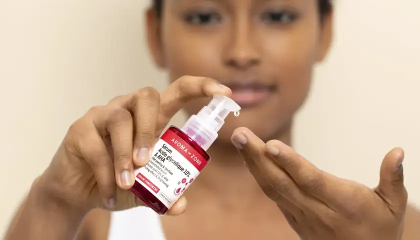 Une goutte de sérum à l'acide glycolique tombe d'une pipette sur le doigt d'une femme.