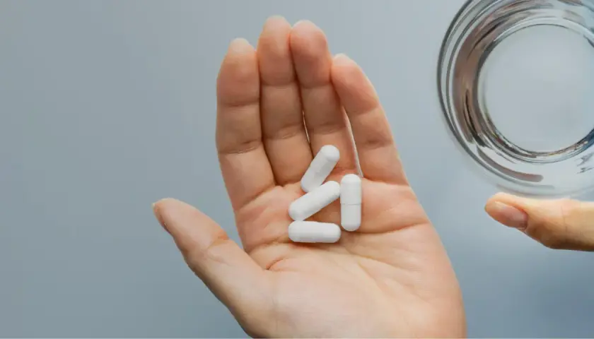 Main ouverte tenant des gélules blanches pour une cure de zinc, à côté d'un verre d'eau.