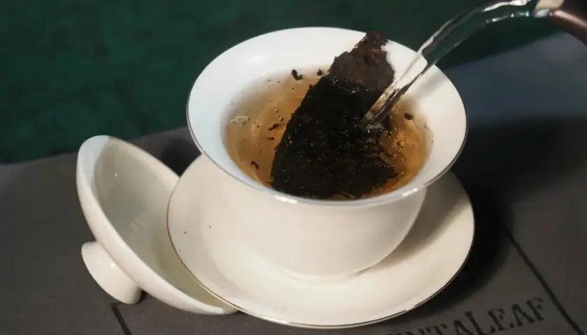 Infusion d'un thé sombre dans une tasse blanche, révélant les fermenté bienfaits. L'eau chaude libère les arômes.