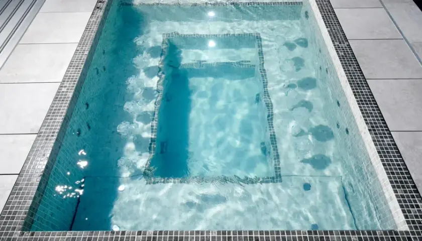 Un jacuzzi moderne avec des jets d'eau, entouré de carrelage et de dalles grises. Le poids d'un jacuzzi rempli d'eau est considérable.
