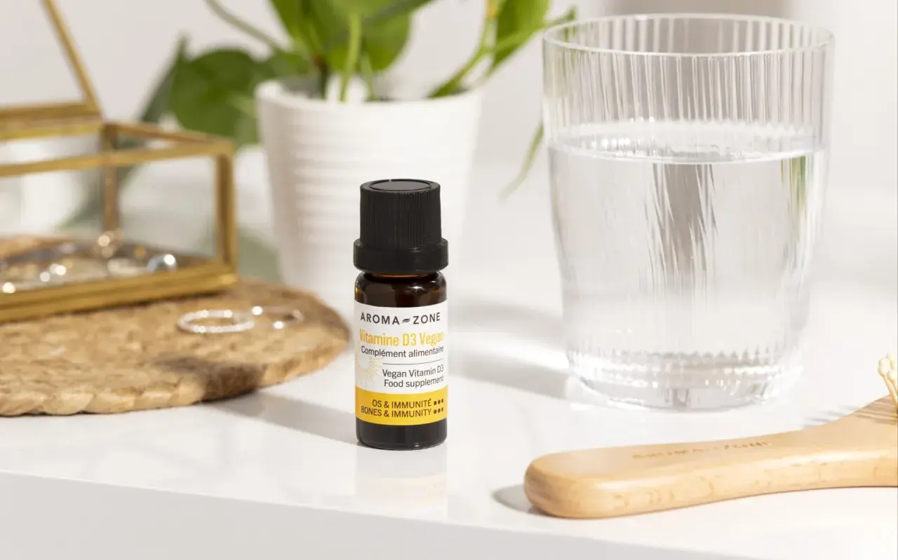 Un remède de grand-mère pour le manque de vitamine D : un flacon de Vitamine D3 Vegan Aroma-Zone, à côté d'un verre d'eau et d'une brosse en bois.