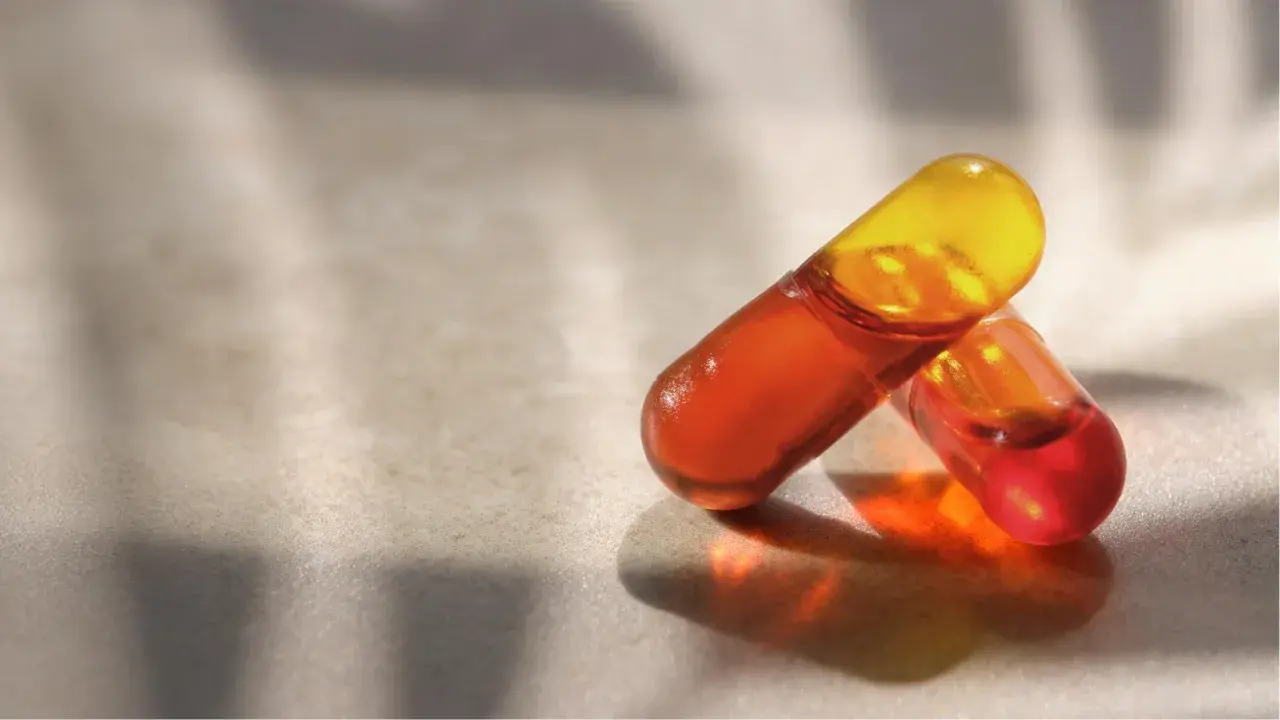 Deux capsules d'huile de krill translucides, aux teintes orangées et jaunes, sur une surface texturée. Découvrez les bienfaits de l'huile de krill.