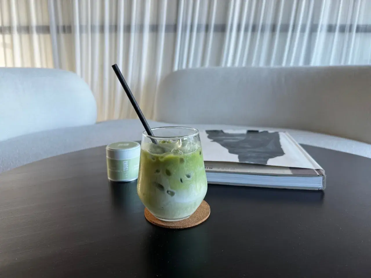 Un verre de thé matcha glacé, crémeux et rafraîchissant, avec une paille noire, à côté d'une boîte de matcha et d'un livre.