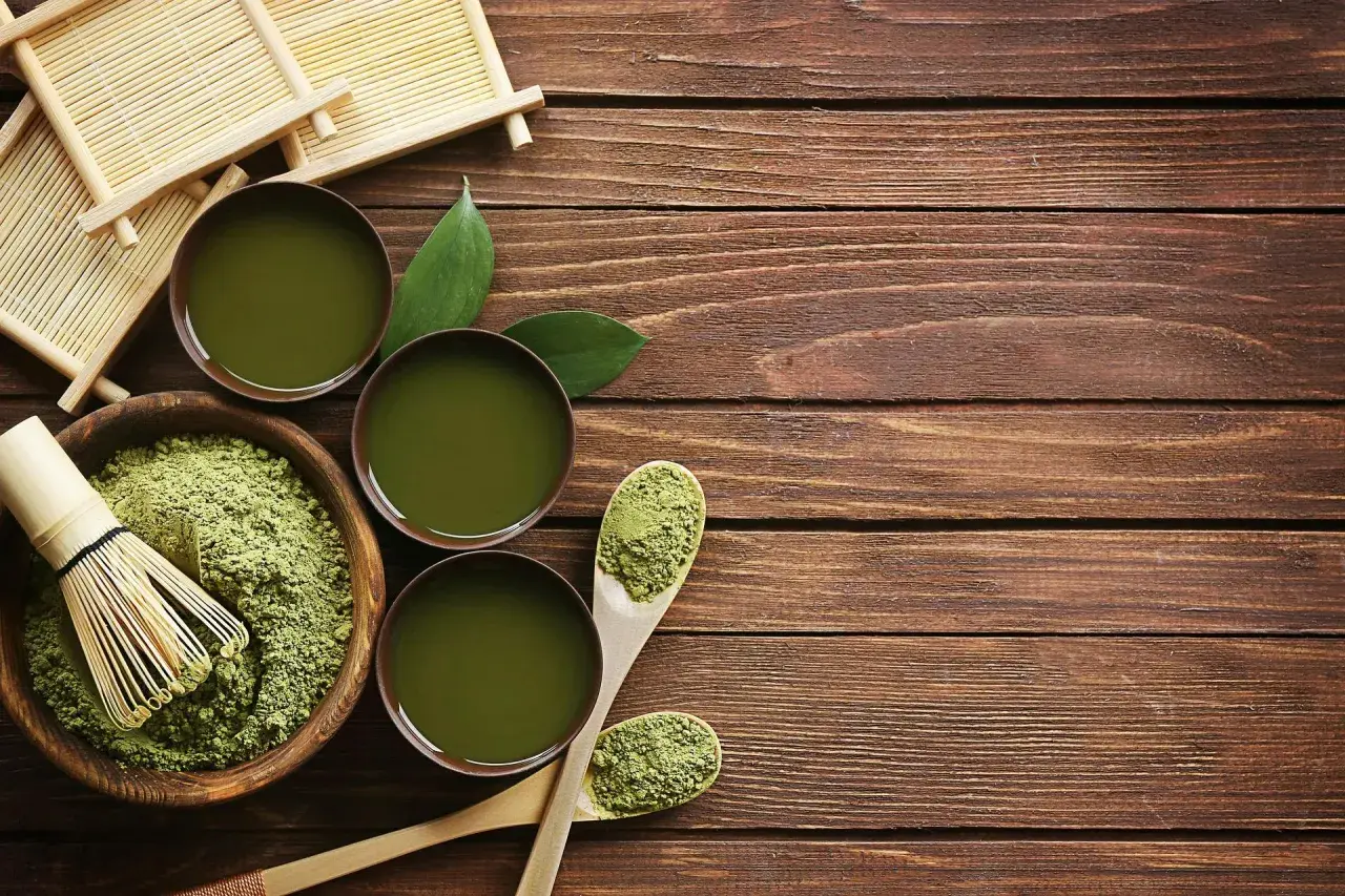 Préparation du matcha : poudre verte, fouet en bambou, bols de thé et cuillères en bois sur une table en bois.