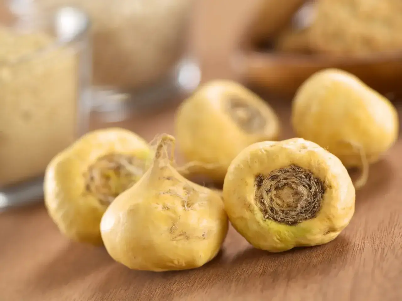 Cinq racines de maca jaunes, entières et séchées, reposent sur une surface en bois.