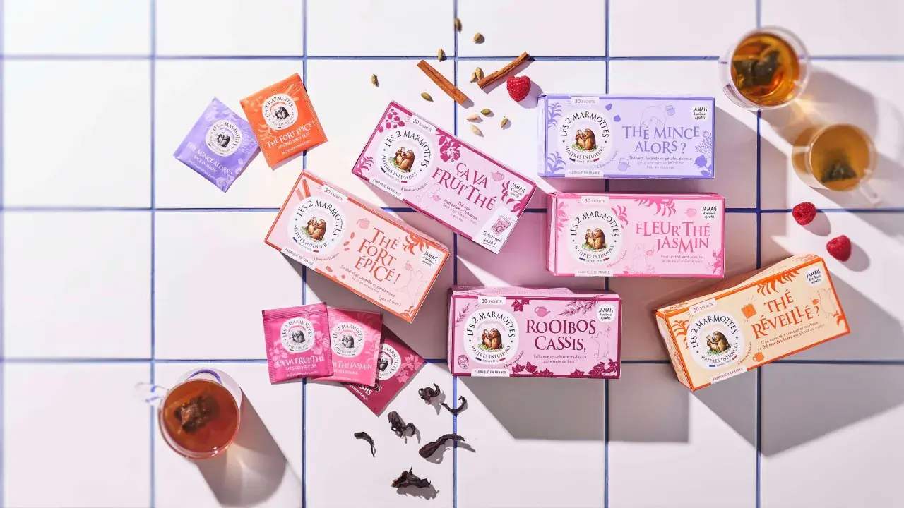 Des boîtes de thé colorées, dont un thé noir "Le Réveille?", disposées sur un carrelage blanc, avec des épices et des fruits rouges.