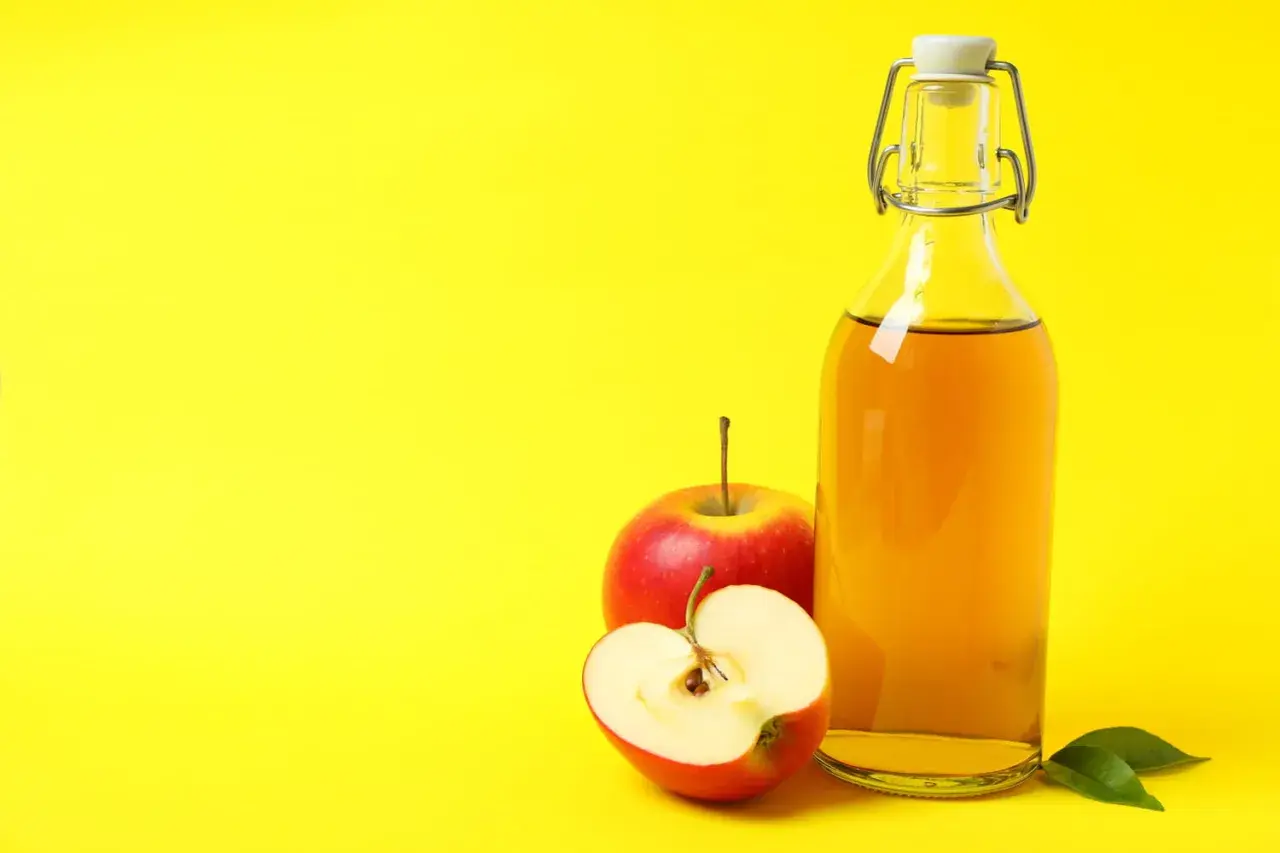 Bouteille de vinaigre de cidre et pommes rouges, suggérant un urticaire traitement naturel.