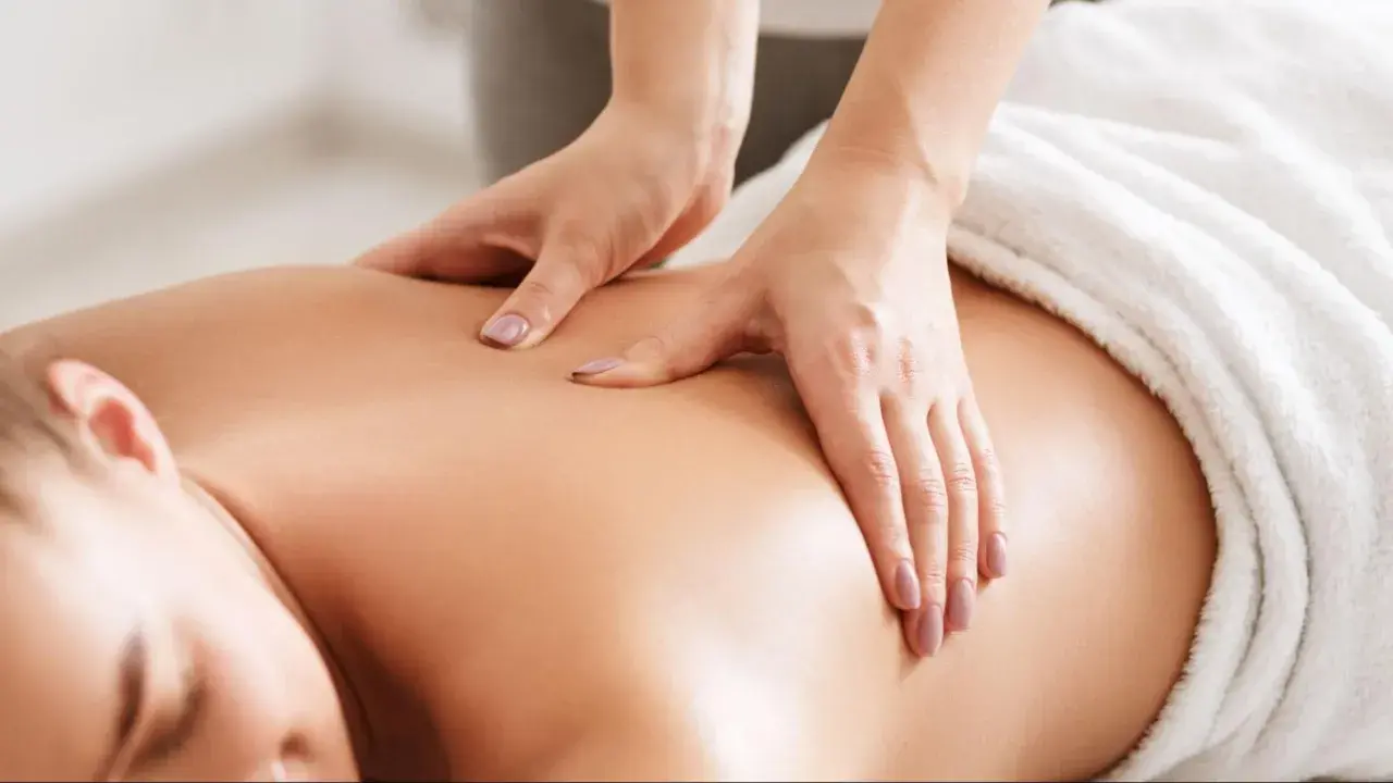 Mains expertes prodiguant un massage relaxant sur le dos d'une personne. Idéal pour savoir que prendre pour aller au spa et se détendre.