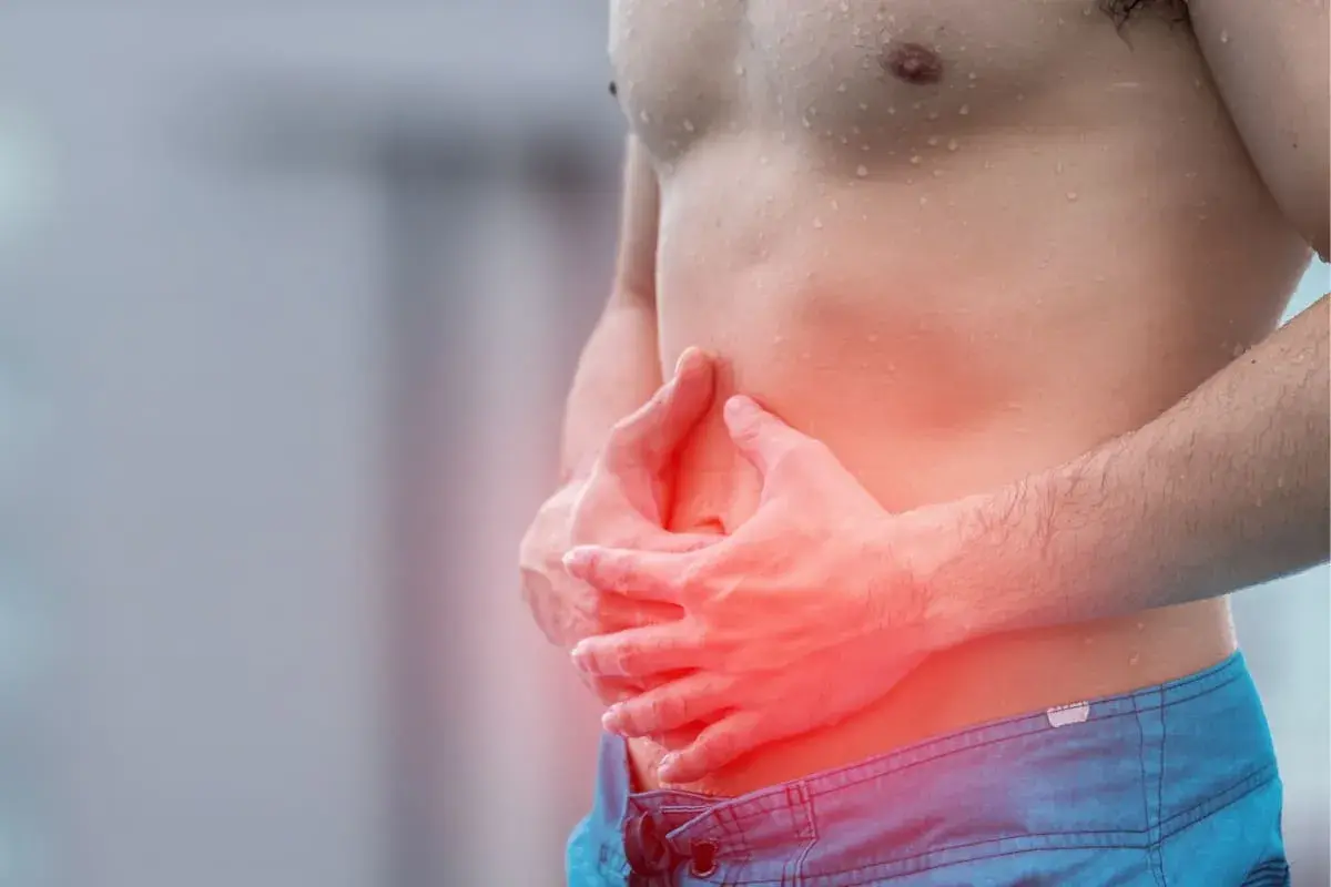 Homme tenant son ventre douloureux, cherchant comment calmer les douleurs d'estomac. La zone rouge indique la douleur.