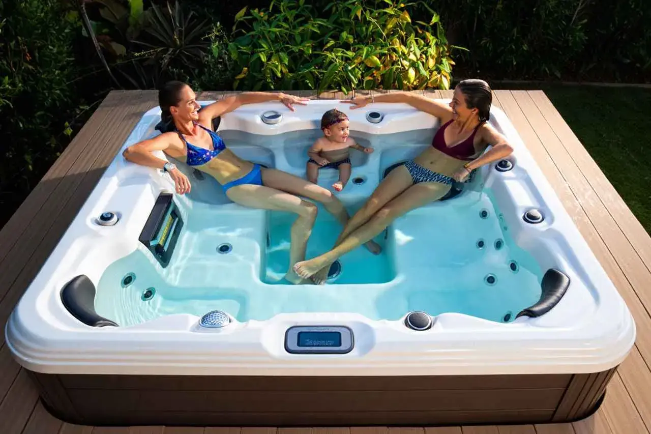Deux femmes et un bébé profitent du bienfait jacuzzi en extérieur, entourés de verdure.