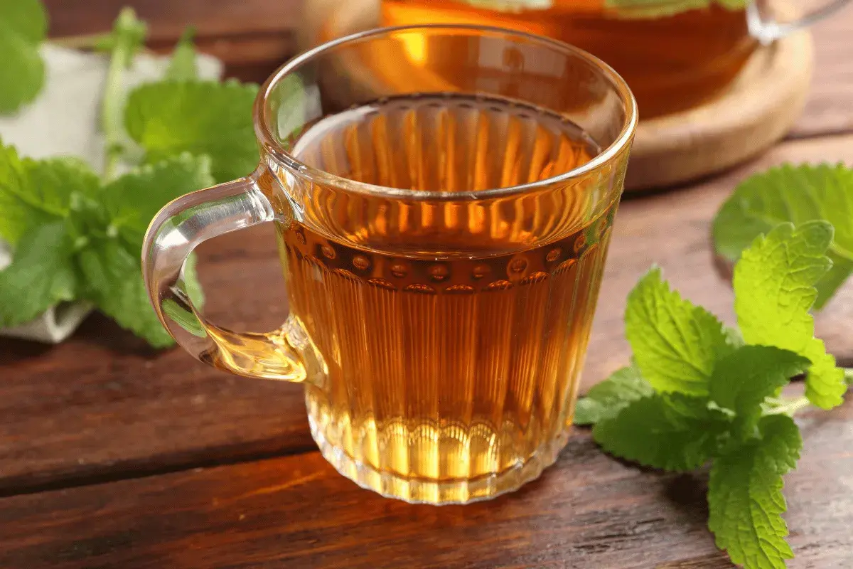 Une tasse de thé ambré, ornée de feuilles de mélisse fraîche, sur une table en bois.