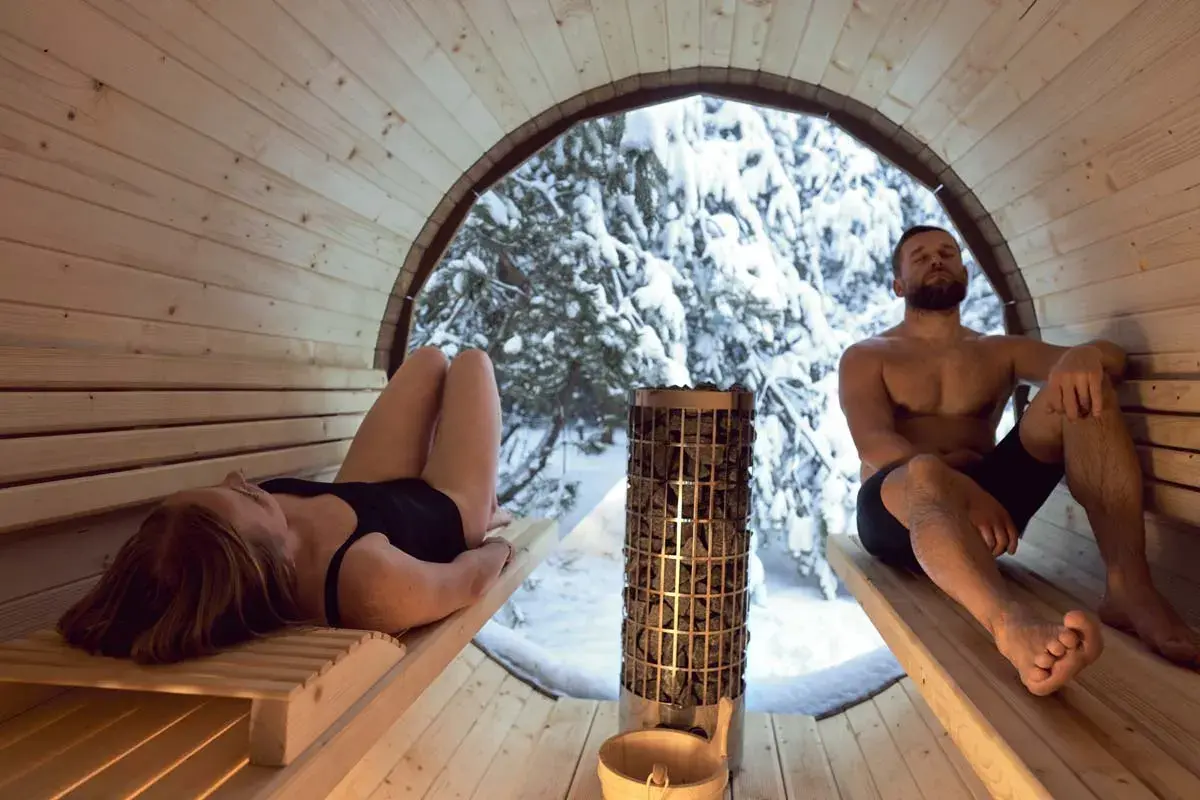 Couple se détendant dans un sauna en bois, avec vue sur une forêt enneigée. Le sauna tous les jours danger, mais ici, c'est un moment de pur bien-être.
