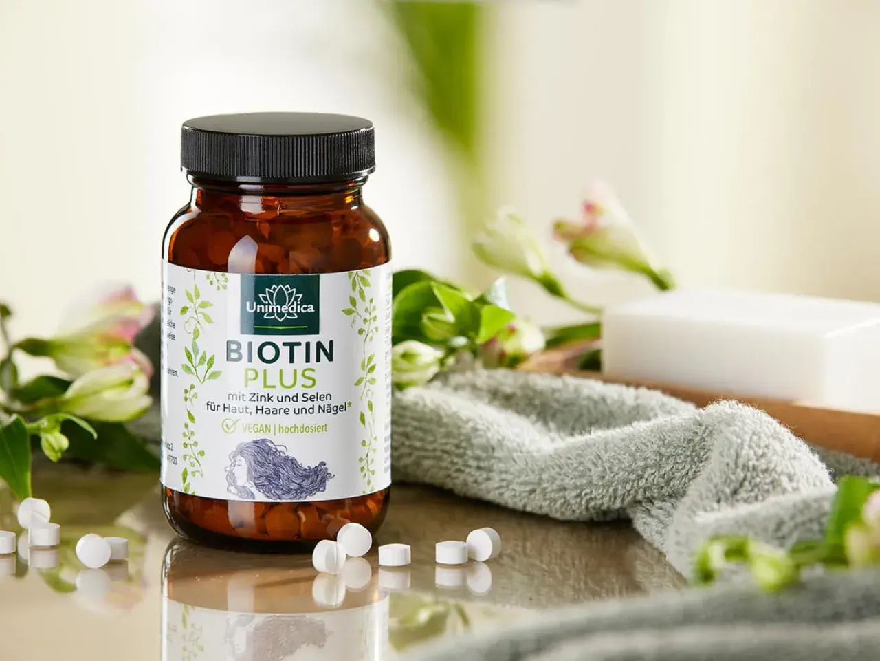 Bouteille de Biotin Plus, un supplément de vitamine B7, entourée de fleurs et d'une serviette douce. Idéal pour la peau, les cheveux et les ongles.