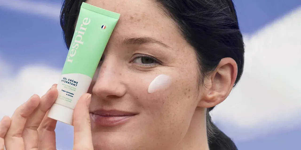 Une femme applique une crème hydratante sur sa joue. Le tube "Respire" est tenu près de son visage, montrant comment hydrater sa peau.