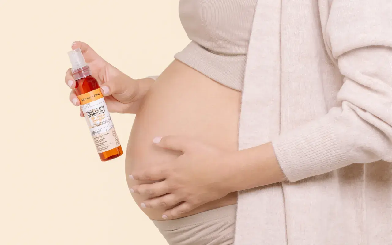 Une femme enceinte tient une huile de soin pour vergetures, idéale pour la grossesse. Le rooibos, ingrédient naturel, prend soin de la peau.