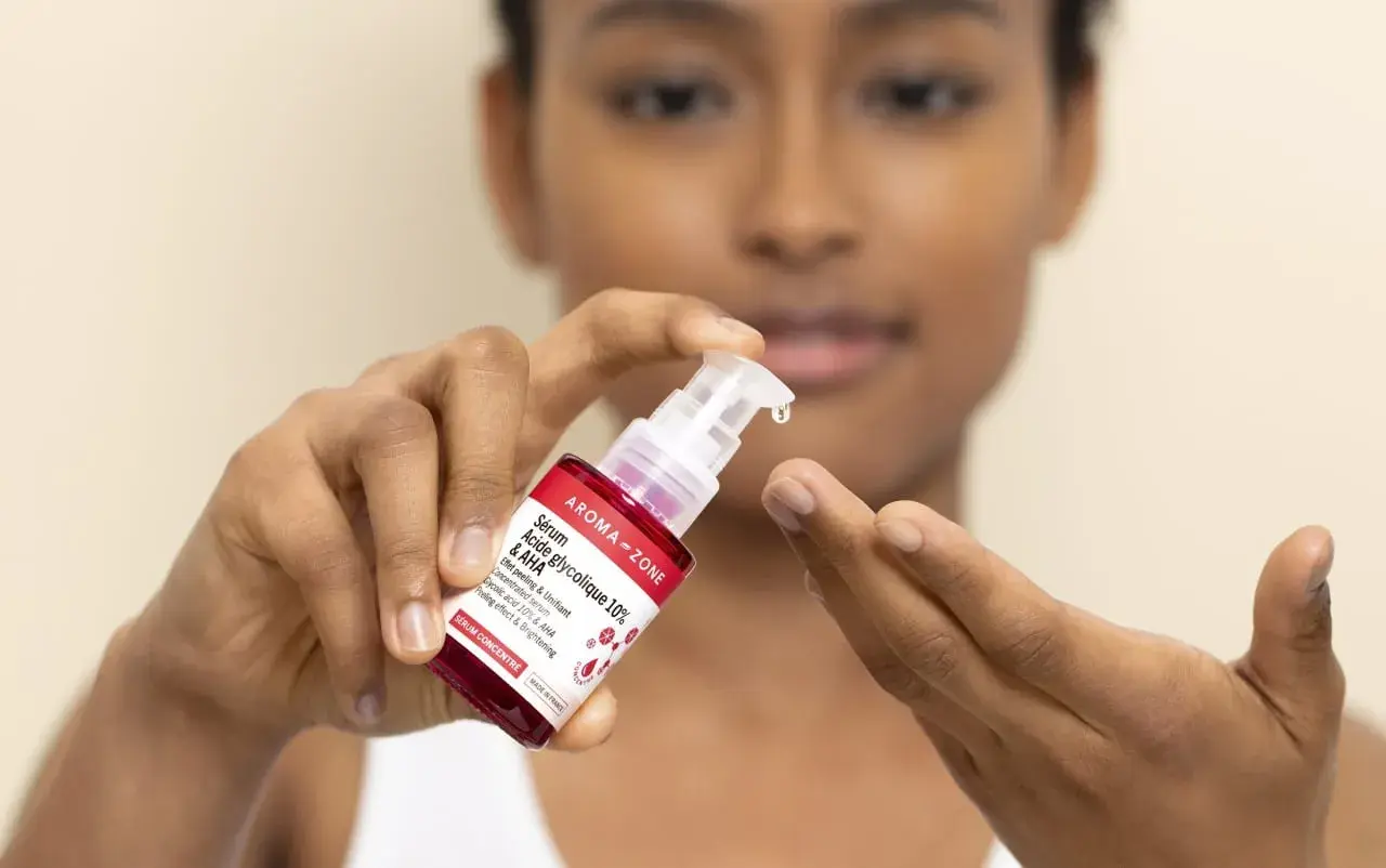Une goutte de sérum à l'acide glycolique tombe d'une pipette sur le doigt d'une femme.
