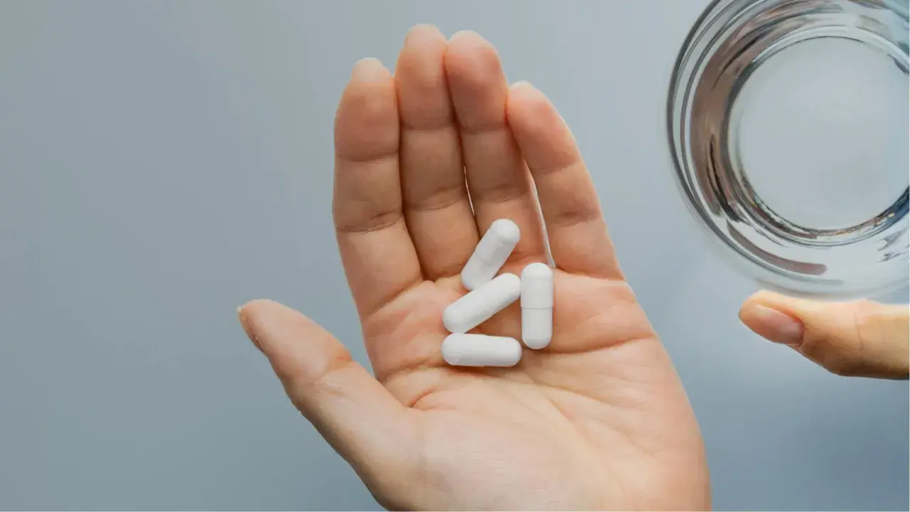 Main ouverte tenant des gélules blanches pour une cure de zinc, à côté d'un verre d'eau.