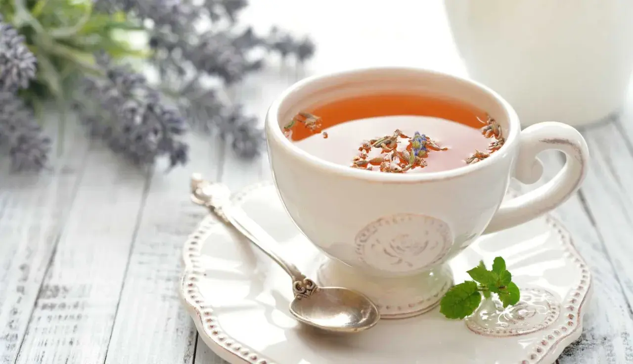Une tasse de thé à la lavande, parfaite pour savoir quel thé boire le soir. Une cuillère ancienne et des brins de menthe complètent la scène.