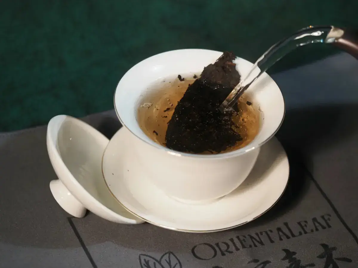 Infusion d'un thé sombre dans une tasse blanche, révélant les fermenté bienfaits. L'eau chaude libère les arômes.