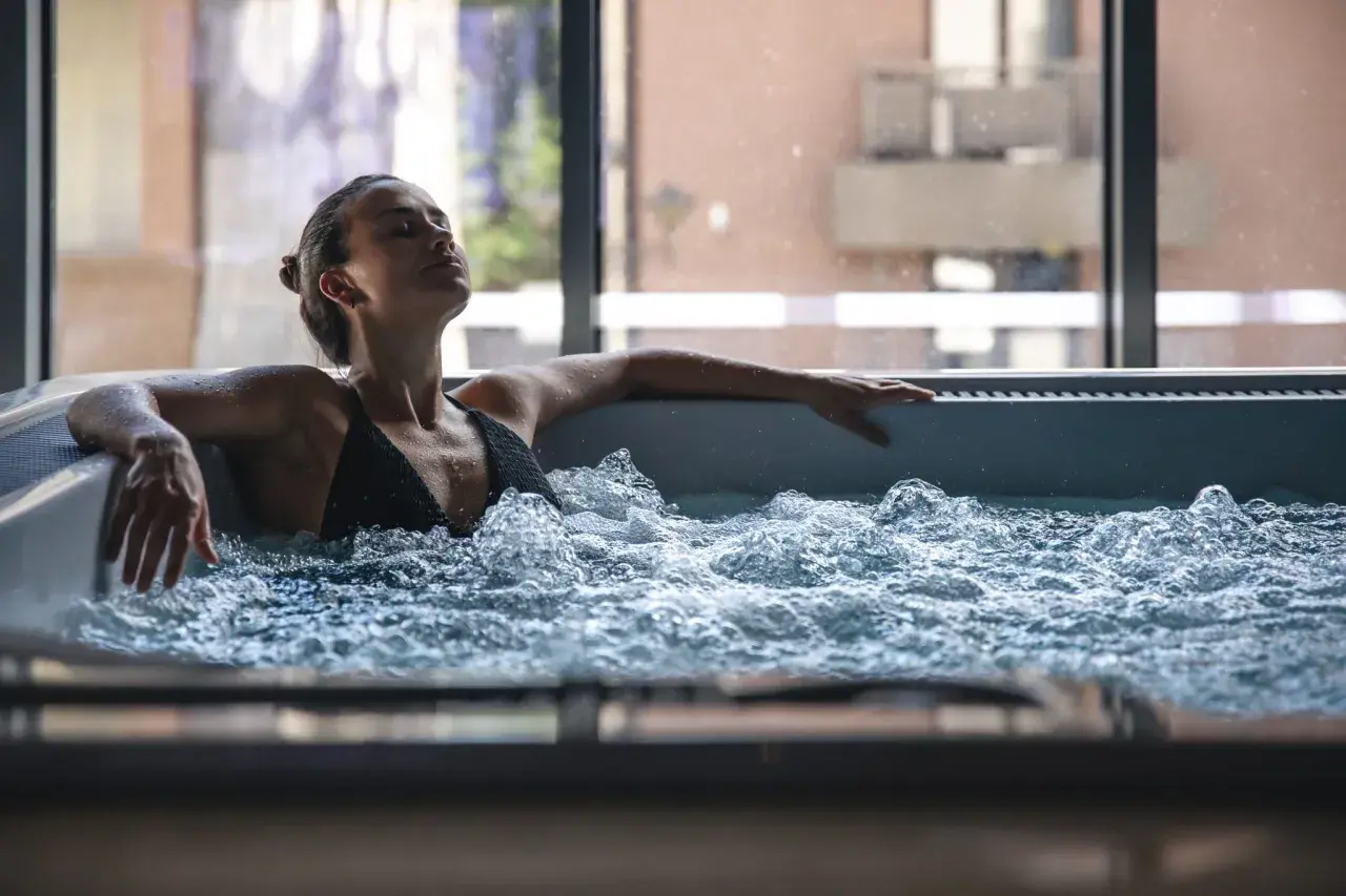 Femme détendue dans un jacuzzi, ignorant les contre-indications possibles. L'eau bouillonnante crée une atmosphère apaisante.