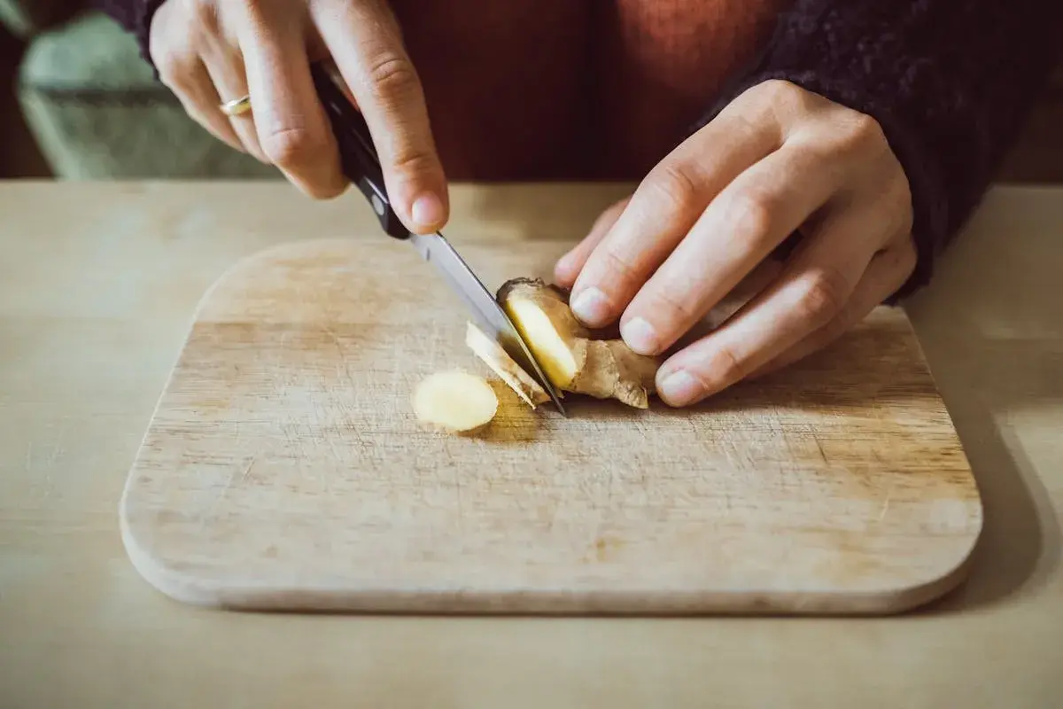 Préparation d'un thé au gingembre le soir. Des mains coupent finement du gingembre sur une planche en bois.