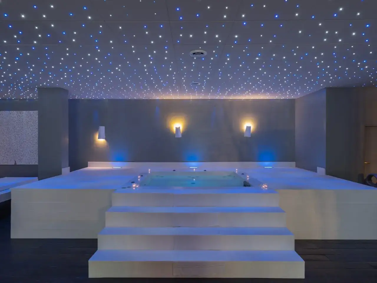 Un espace détente avec un bassin d'eau illuminé par des lumières bleues et un plafond étoilé. Ce chromothérapie spa invite à la relaxation.