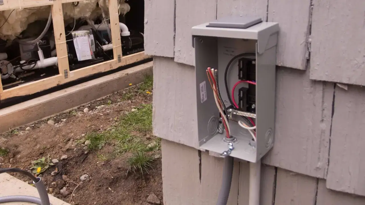 Boîtier électrique ouvert sur le côté d'une maison, prêt pour le branchement spa gonflable. Câbles visibles à l'intérieur.