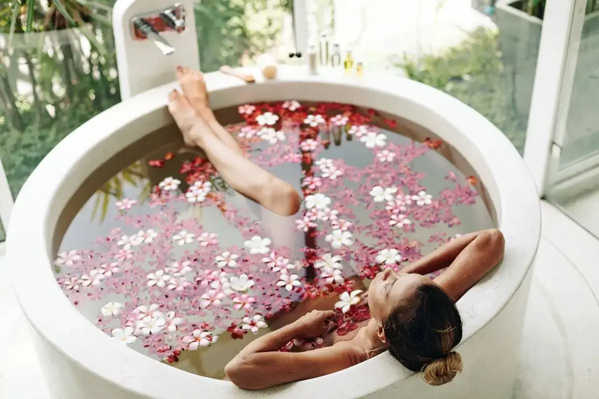 Une femme se détend dans une baignoire remplie de fleurs, mais attention aux dangers du spa : chaleur excessive, produits chimiques, infections.