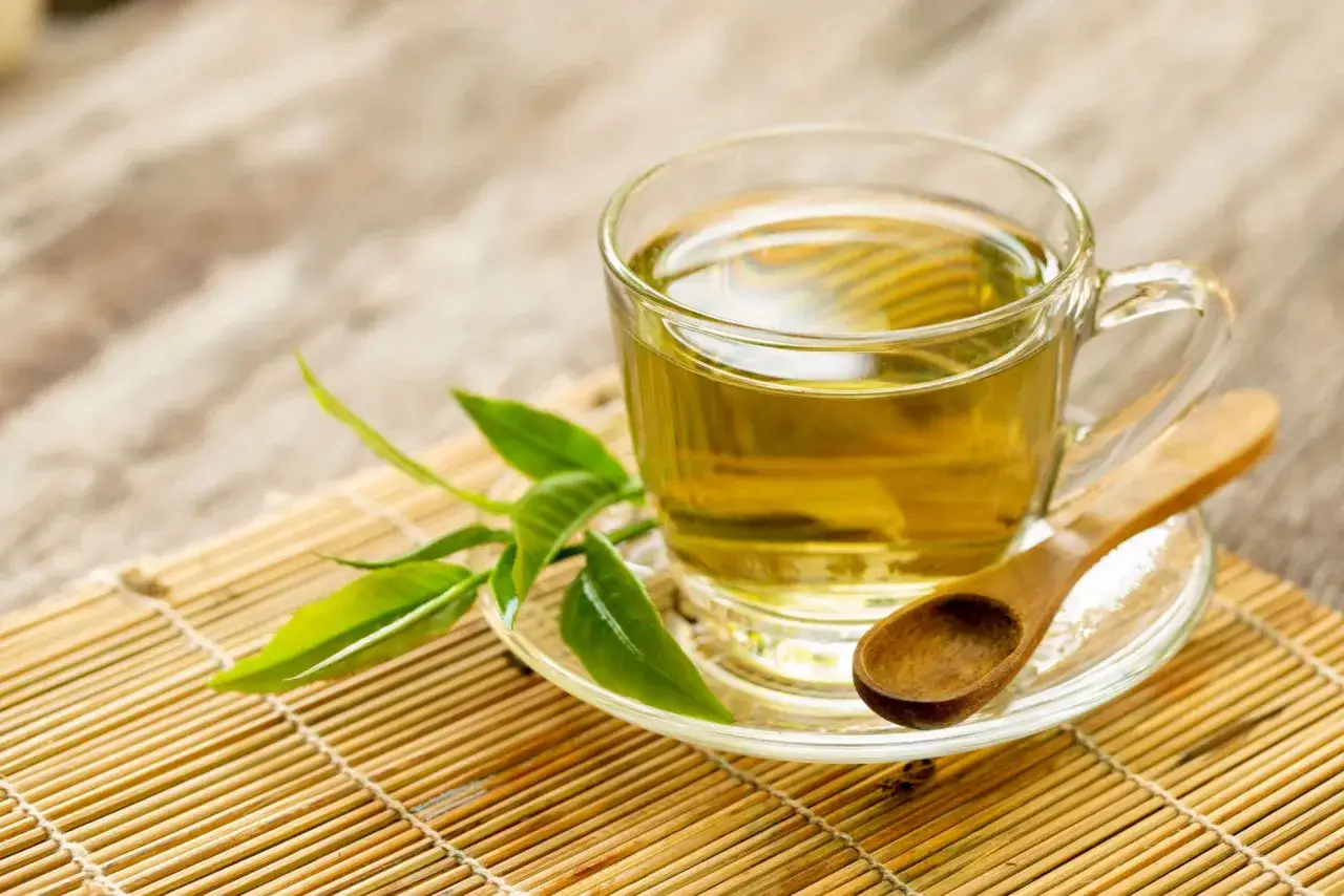 Une tasse de tisane verveine dor&eacute;e, avec des feuilles fra&icirc;ches et une cuill&egrave;re en bois sur un tapis de bambou.