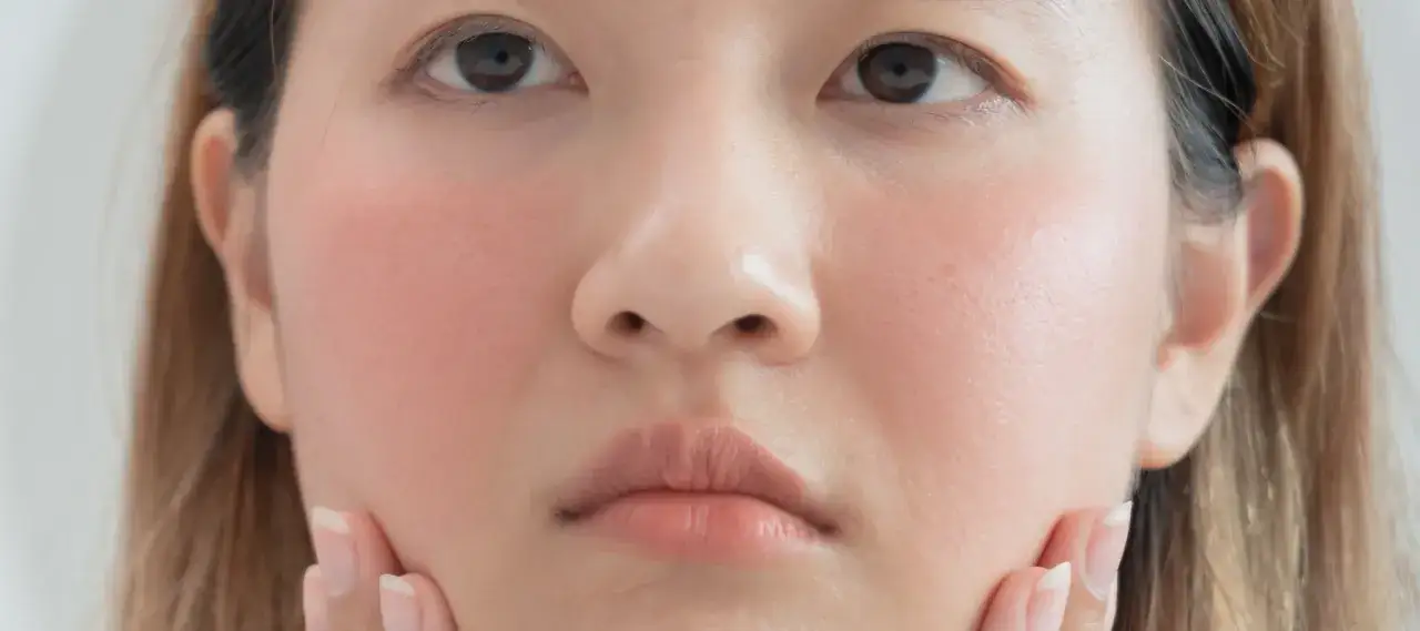Gros plan sur le visage d'une jeune femme, ses joues ros&eacute;es et ses l&egrave;vres doucement effleur&eacute;es par ses doigts.