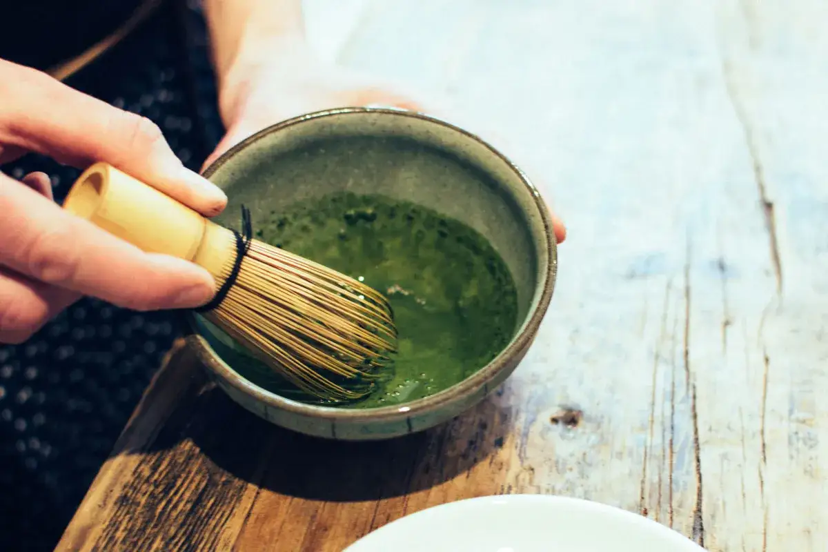 Préparation d'un matcha crémeux avec un fouet en bambou. La poudre verte se mélange à l'eau dans un bol en céramique.