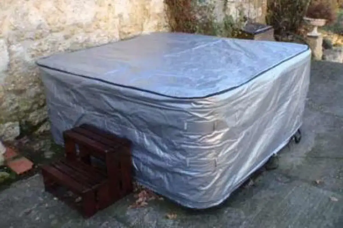 Spa rigide bâché pour l'hivernage, prêt à affronter le froid. Des marches en bois sont à côté.
