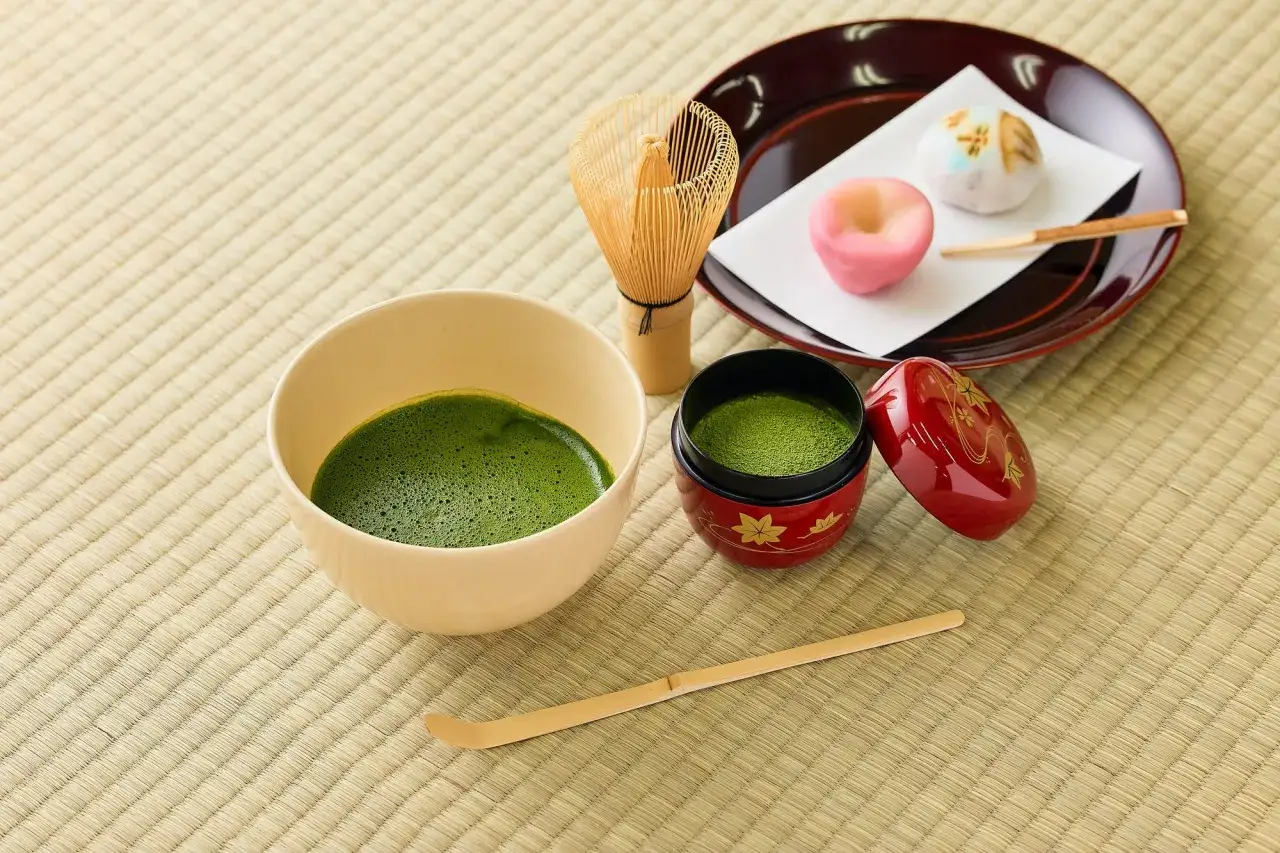 Préparation du matcha : la quantité de matcha par tasse est idéale pour une boisson onctueuse. Un fouet, une cuillère et des douceurs japonaises complètent la scène.