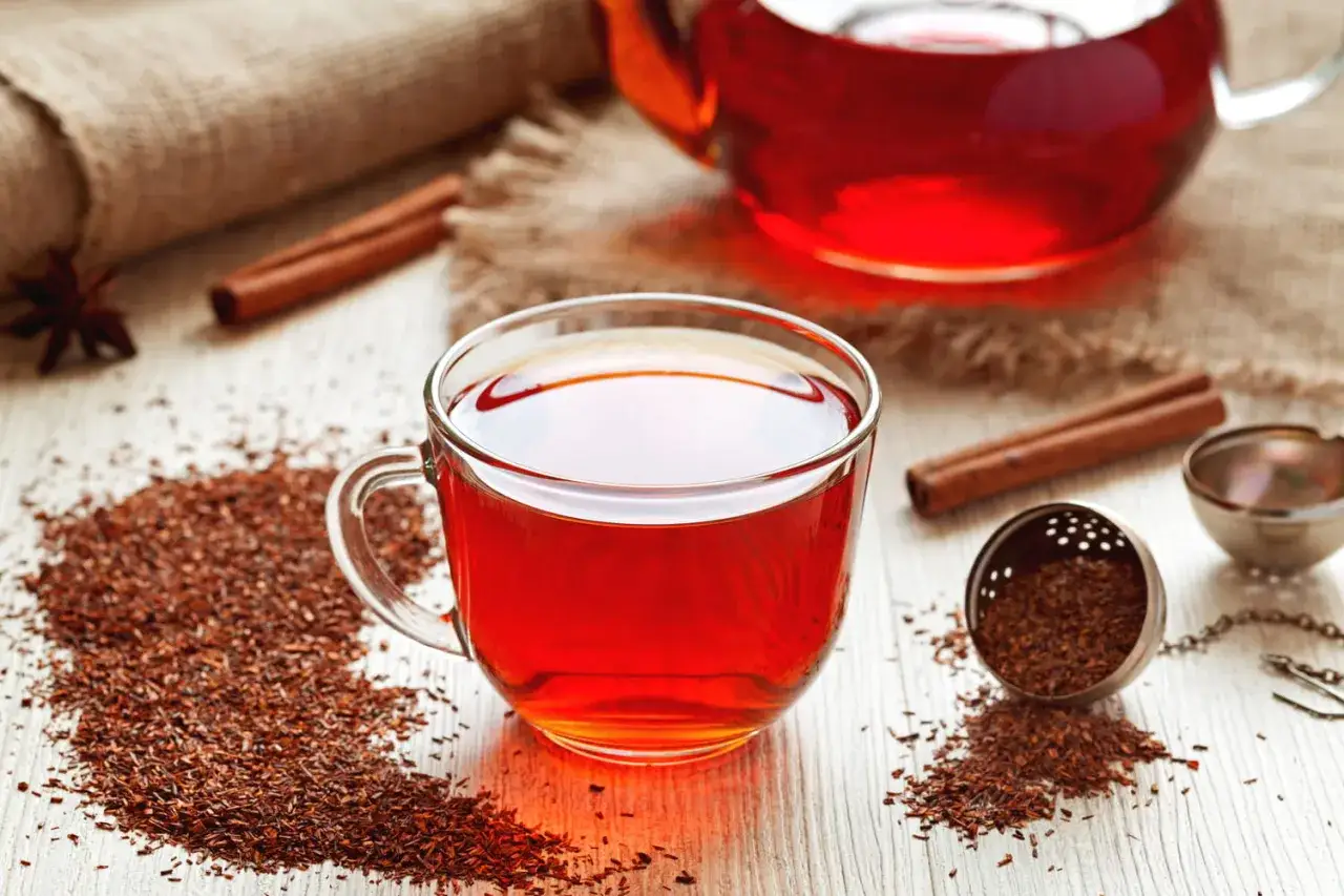 Une tasse de th&eacute; rooibos, parfait pour la grossesse, avec des b&acirc;tons de cannelle et des feuilles de th&eacute; sur une table en bois.