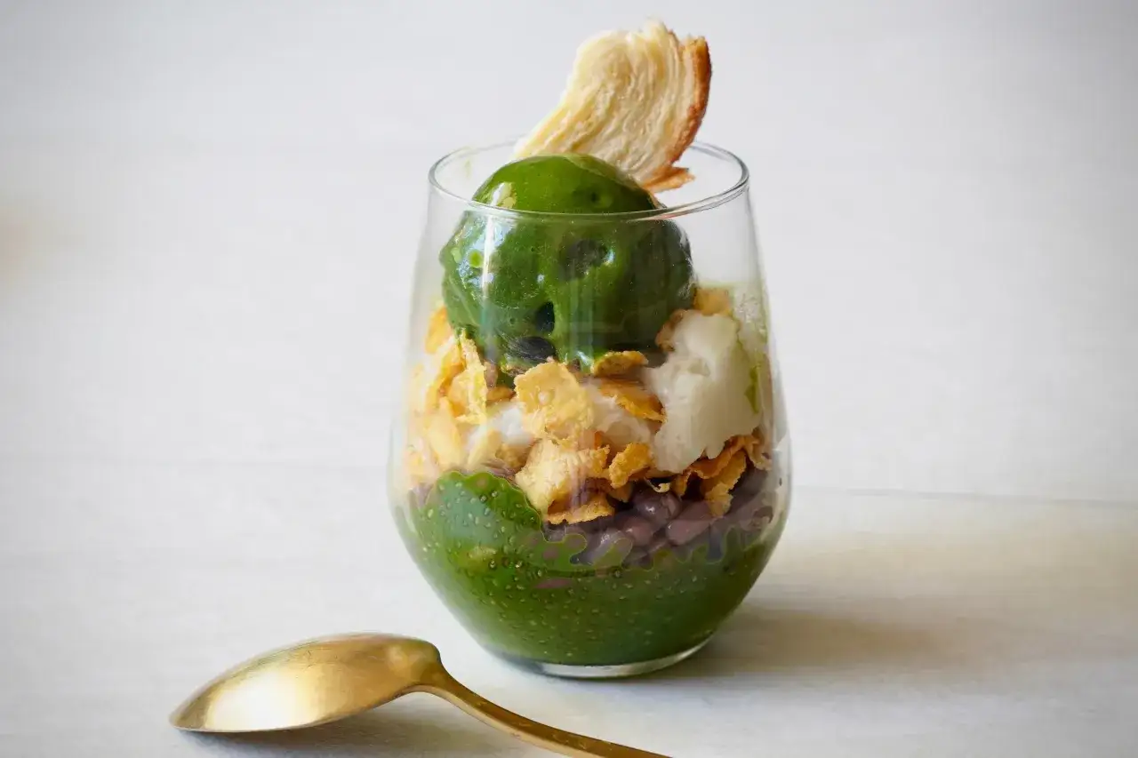 Un d&eacute;lice vert et croquant : une coupe garnie de haricots rouges, de c&eacute;r&eacute;ales, d'une boule de glace et d'une touche de th&eacute; matcha, surmont&eacute;e d'une feuille croustillante.