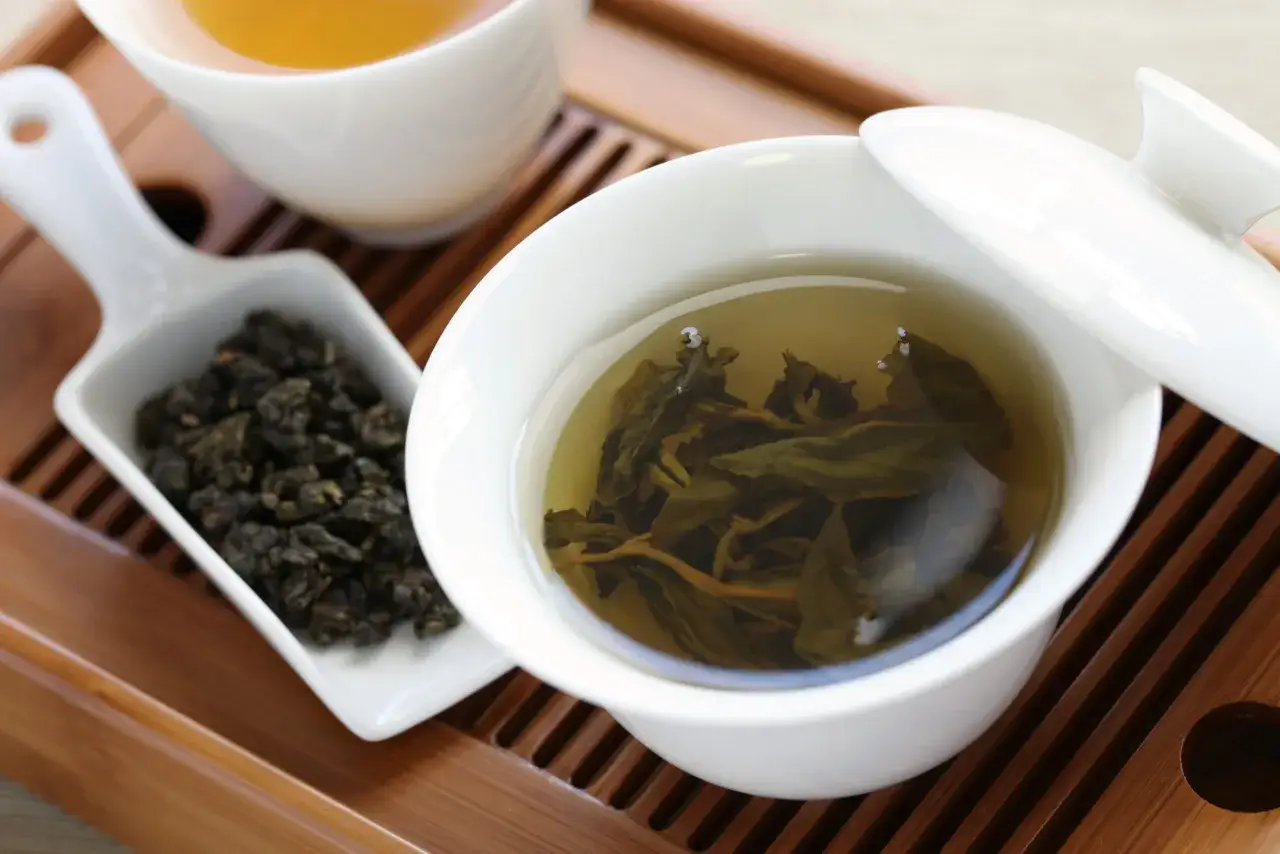 Tasses de th&eacute; oolong sur un plateau en bois. Les feuilles infus&eacute;es flottent dans la tasse, un effet secondaire apaisant de cette boisson.