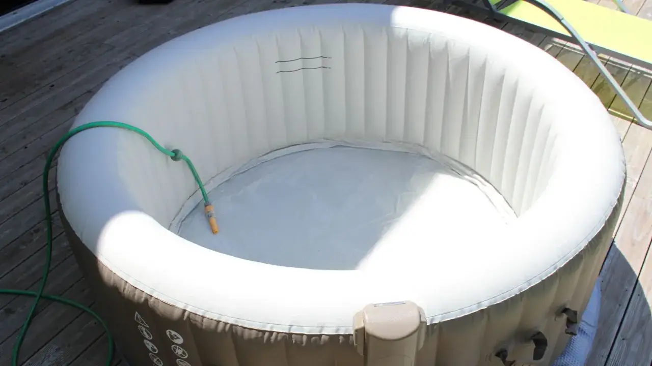 Un spa gonflable vide sur une terrasse en bois, avec un tuyau d'arrosage prêt à le remplir. Peut-on laisser un spa sans eau ? Oui, pour le nettoyage ou le rangement.