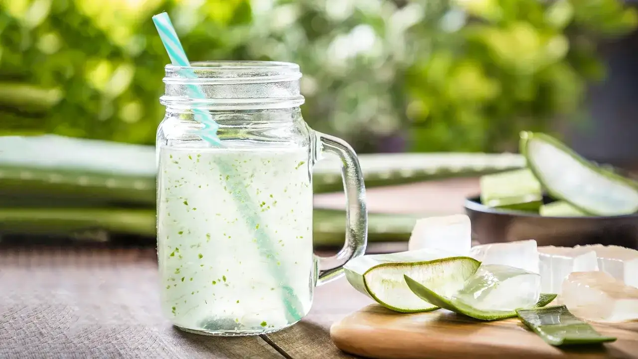 Un verre de aloe vera à boire rafraîchissant, avec des morceaux d'aloe vera frais sur une planche en bois.